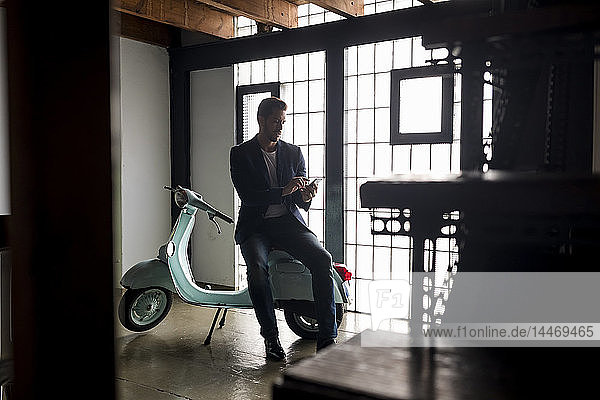Mann mit Motorroller auf einem Dachboden mit Mobiltelefon