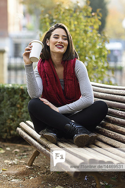 Porträt einer lächelnden jungen Frau  die sich mit Kaffee entspannt  um auf eine Bank zu gehen