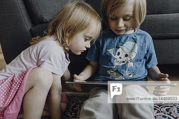 Bruder und kleine Schwester sitzen zu Hause auf dem Boden und benutzen ein digitales Tablett