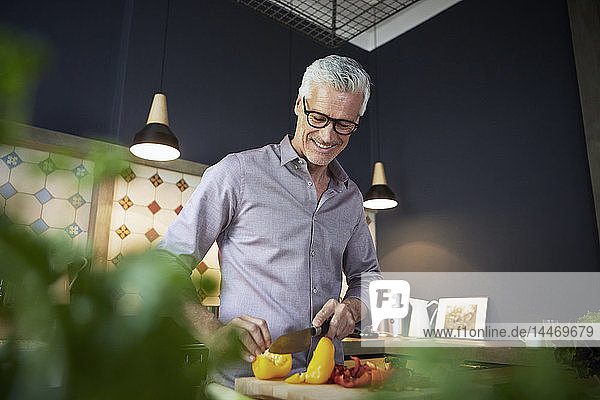 Smiling mature man chopping bell pepper in kitchen