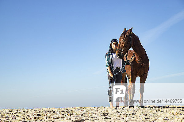 Frau mit Pferd im Sand stehend