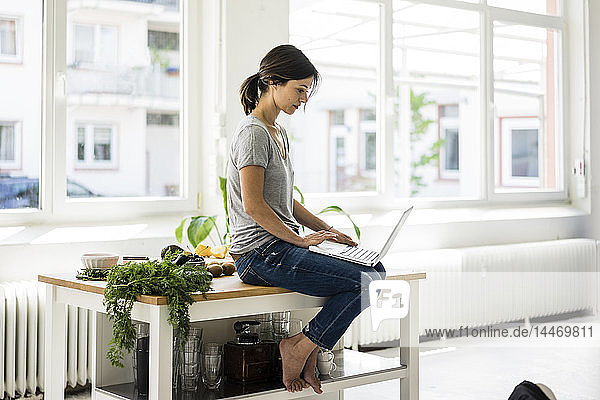 Woman sitting on kitchen table  searching for healthy recipes  using laptop