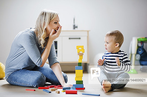 Glückliche Mutter und Kleinkind spielen zu Hause mit Bauklötzen