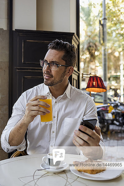 Geschäftsmann beim Frühstück in einem Café mit Handy in der Hand