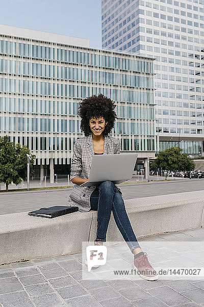 Porträt einer lächelnden Geschäftsfrau  die mit einem Laptop vor dem Bürogebäude arbeitet