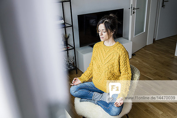 Reife Frau sitzt im Schneidersitz mit geschlossenen Augen im Schneidersitz und meditiert zu Hause
