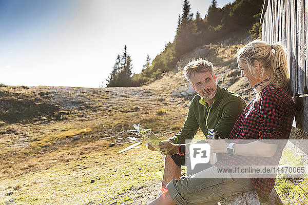 Hiking couple sitting in front of mountain hut  taking a break  holding map