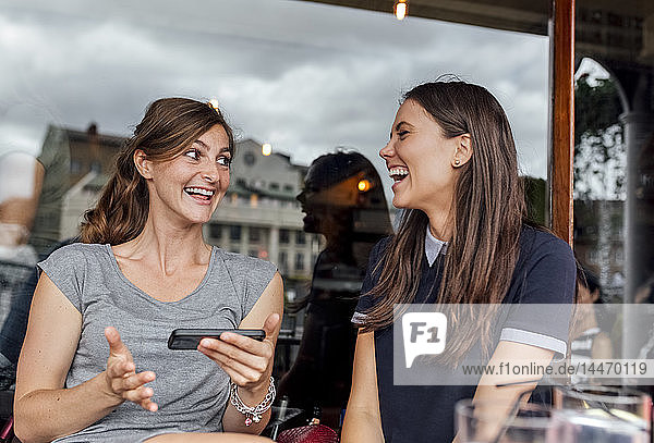 Zwei Frauen amüsieren sich auf einer Terrasse mit ihrem Smartphone