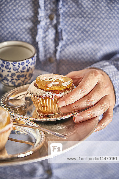 Woman's hand holding muffin with candied orange slice on silver platter