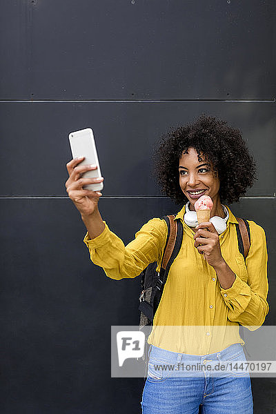 Porträt einer lächelnden Frau mit Eistüte  die sich mit einem Smartphone selbstständig macht