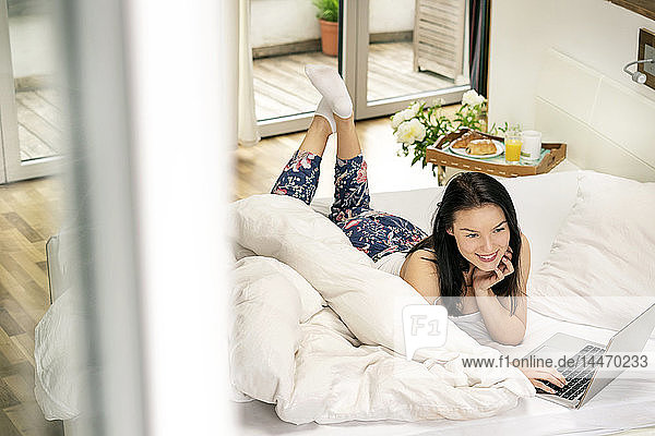 Junge Frau im Bett liegend  morgens mit Laptop