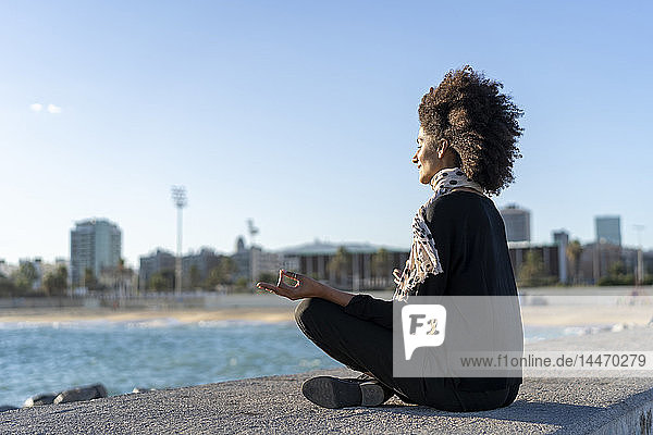 Spanien  Barcelona  Frau meditiert auf einer Mauer nahe dem Meer