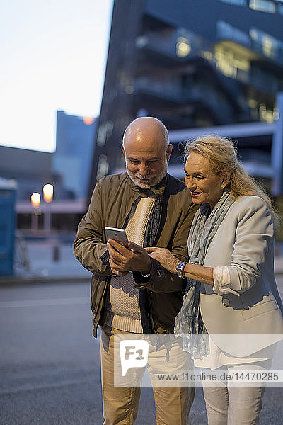 Spain  Barcelona  senior couple sharing cell phone in the city at dusk