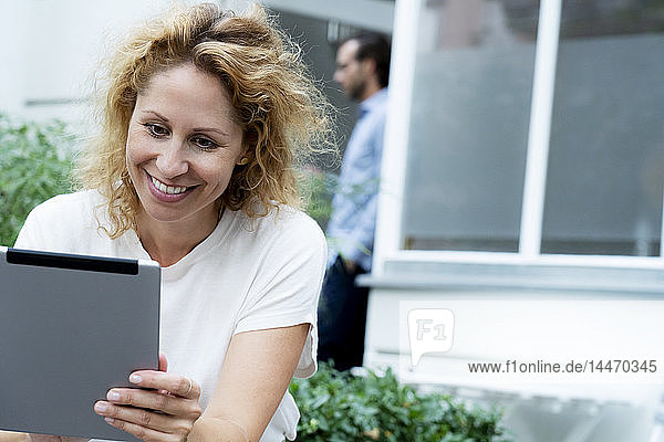 Lachende Frau  die an ihrem digitalen Tablet arbeitet und im Garten sitzt