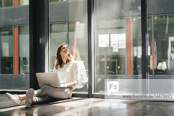 Geschäftsfrau sitzt am Boden in einem leeren Büro und benutzt einen Laptop