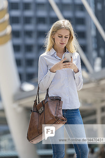 Blonde Frau mit Handtasche überprüft Mobiltelefon in der Stadt