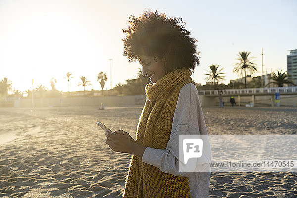 Frau mit gelbem Schal  mit Smartphone am Strand