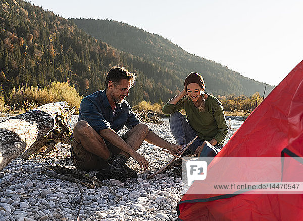 Mature couple camping at riverside with wood for a camp fire