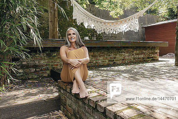 Porträt einer lächelnden Frau  die barfuss auf der Terrasse im Hinterhof sitzt