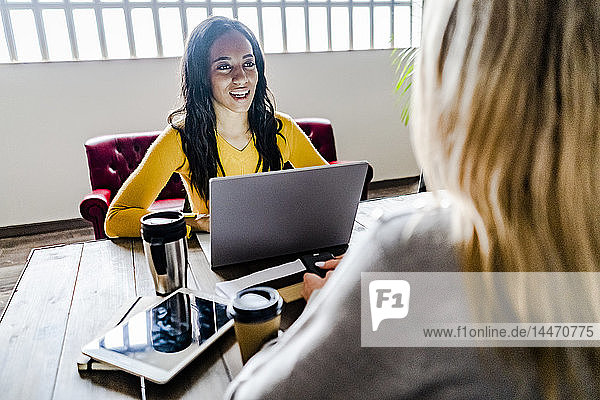 Two young businesswomen talking at conference table in office