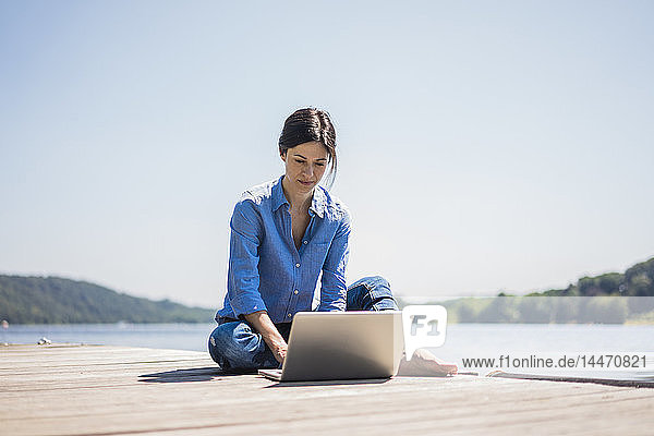 Reife Frau  die an einem See arbeitet  mit Laptop auf einem Steg