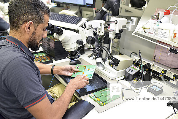 Mann  der ein Mikroskop für die Qualitätskontrolle bei der Herstellung von Leiterplatten für die Elektronikindustrie benutzt