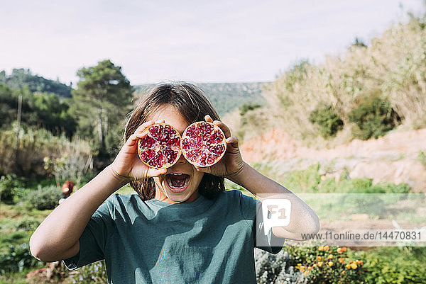 Boy standing in the countryside  covering eyes with halved pomegranates