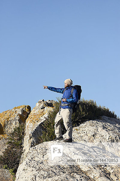 Spanien  Andalusien  Tarifa  Mann auf Wanderung  steht auf einem Felsen und zeigt mit dem Finger