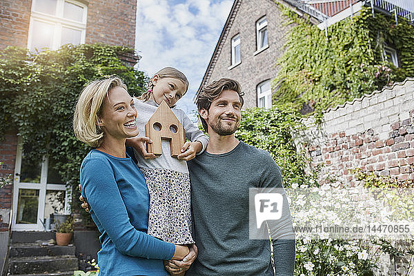 Porträt einer glücklichen Familie vor ihrem Haus mit Hausmodell