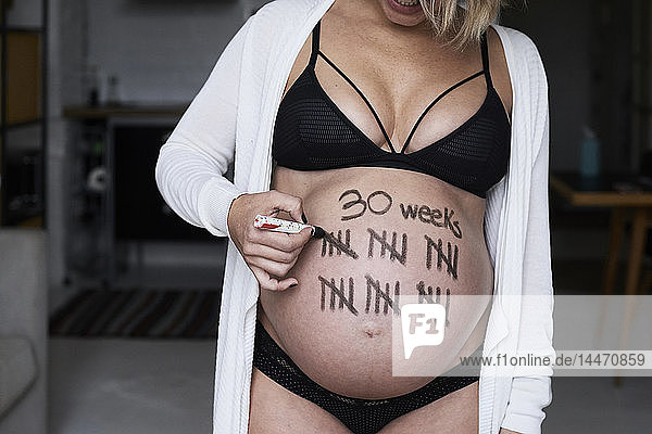 Close-up of pregnant woman painting tally marks on her belly
