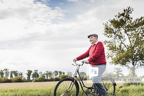 Älterer Mann schiebt Fahrrad in ländlicher Landschaft