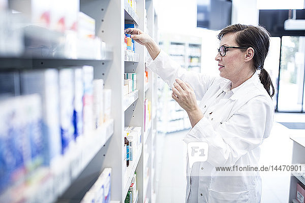Pharmacist sorting medicine at shelf in pharmacy