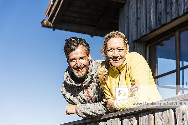 Lächelndes  auf dem Balkon einer Berghütte lehnendes Paar