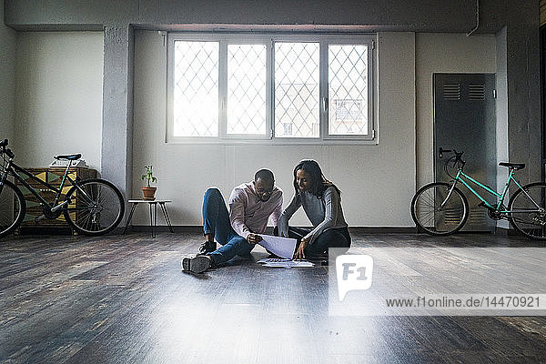 Businessman and businesswoman sitting on the floor discussing documents