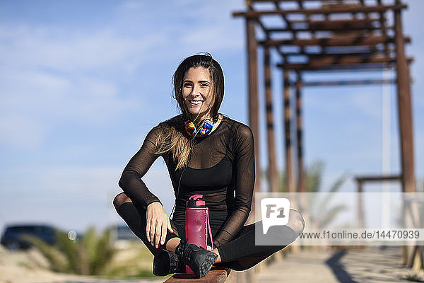 Lächelnde sportliche Frau  die sich nach dem Sport ausruht und auf einer Holzbrücke sitzt