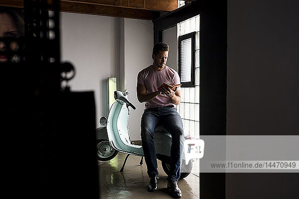 Mann mit Motorroller beim Lesen eines Buches auf einem Dachboden