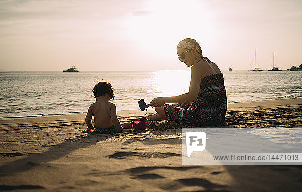 Thailand  Koh Lanta  Mutter spielt mit kleiner Tochter am Strand bei Sonnenuntergang
