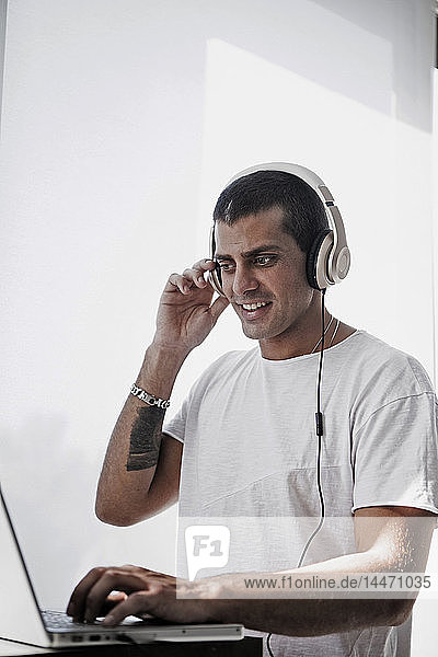 Smiling young man wearing headphones and using laptop