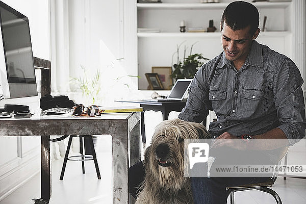 Junger Mann sitzt am Schreibtisch und streichelt Hund