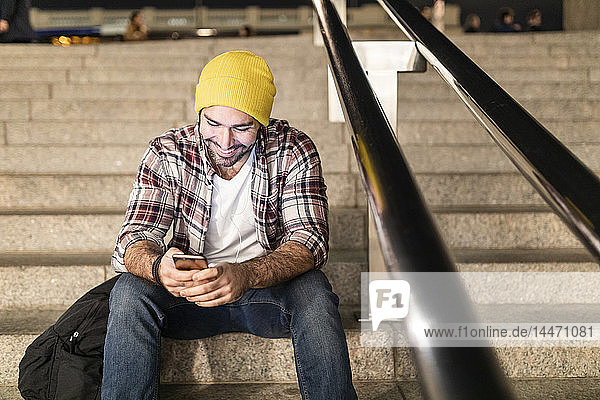 Großbritannien  London  Mann sitzt auf einer Treppe und schaut auf sein Telefon  während er nachts pendelt