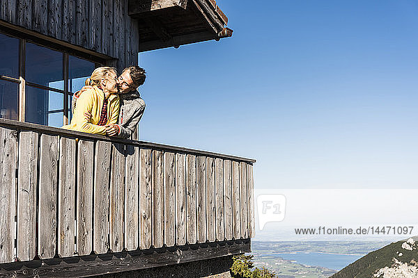 Paar lehnt auf dem Balkon einer Berghütte und küsst sich