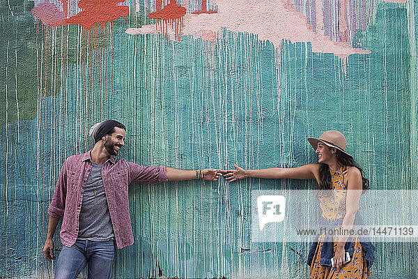 Happy young couple at a wall reaching for each other