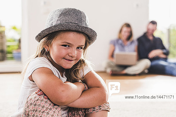 Kleines Mädchen mit Hut  Eltern mit Laptop im Hintergrund