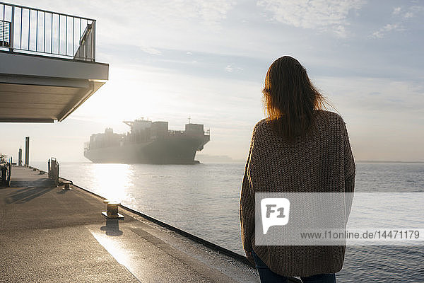 Deutschland  Hamburg  Frau auf der Pier am Elbufer stehend mit Containerschiff im Hintergrund