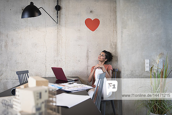 Geschäftsfrau sitzt am Tisch in einem Loft unter einem Herz an einer Betonwand