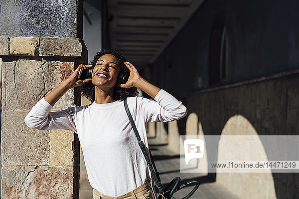 Junge lockere Geschäftsfrau mit Smartphone und Kopfhörern in der Stadt