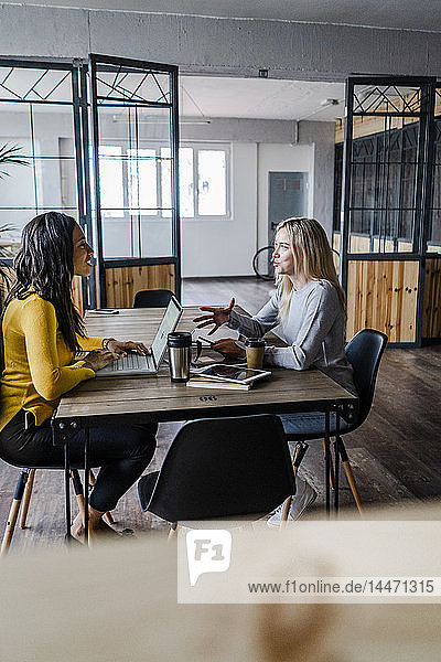 Two young businesswomen talking at conference table in loft office