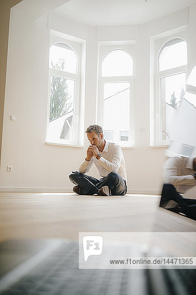 Geschäftsmann in frisch renoviertem Haus  im Schneidersitz auf dem Boden sitzend  mit Laptop im Vordergrund