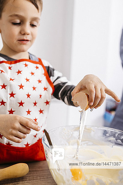 Boy throwing an egg into glass bowl for preparing dough