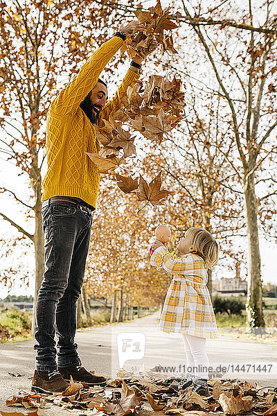 Vater und Tochter genießen im Herbst einen Vormittag im Park und werfen Herbstblätter